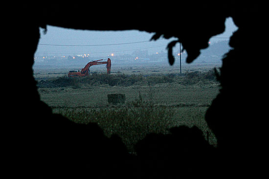 13일 오후 '팽성주민대책위'와 정부가 최종 이주여건에 합의한 가운데 대추리 들녘에 세워놓은 상징물 뒤로 갑작스레 내린 비로 성토공사를 중단한 포크레인이 보인다. [사진-통일뉴스 김주영 기자]
