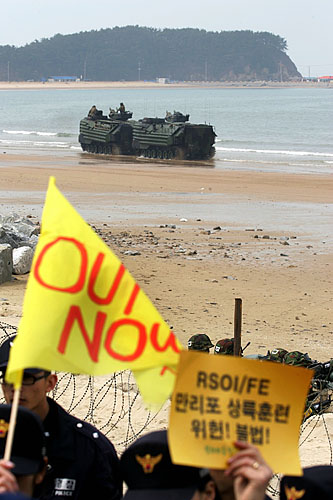 시위대의 훈련반대 피켓 뒤로 훈련중인 장갑차들이 보인다. [사진-통일뉴스 김주영 기자]