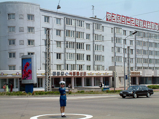 평양 시내 도로의 교통안전원 뒤로 김정일, 김일성화(花) 선전물이 보인다.[사진-통일뉴스 김양희객원기자]
