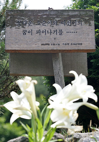'꽃다운 효선이와 미선이의 꿈이 피어나길...'. 추모비 뒤로 2002년 8월에 세워진 자통협 추모순례단의 표지판이 새하얀 백합과 함께 심어져 있다. [사진-통일뉴스 김주영 기자]