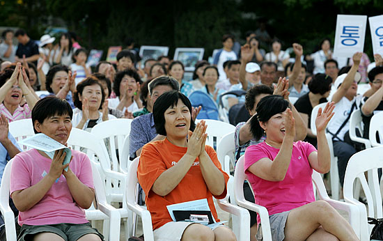 '일찍 찾아온 더위, 통일노래 한자락으로 싹~!'. 더위를 잊은 채 이웃들의 통일노래를 응원하는 주민들.  [사진-통일뉴스 김주영 기자]