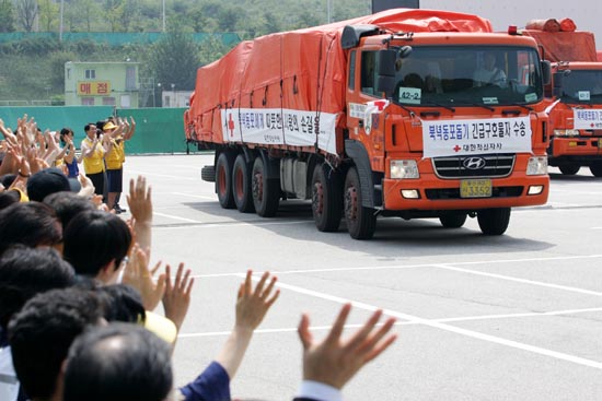 23일 오후 정부의 대북 수해 긴급구호물품 첫 분량이 육로를 통해 북으로 향한 가운데 긴급구호물자를 실은 트럭 40대가 대한적십자사 봉사단의 환송을 받으며 출발하고 있다. [사진-통일뉴스 김주영 기자]