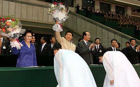 노무현 대통령과 권양숙 여사가 환영의 꽃다발을 받아들고 관중들의 환호에 화답하고 있다. 이날 김정일 위원장은 나오지 않았고 김영남 상임위원장이 노무현 대통령과 함께 자리했다. [사진-청와대 사진기자단]