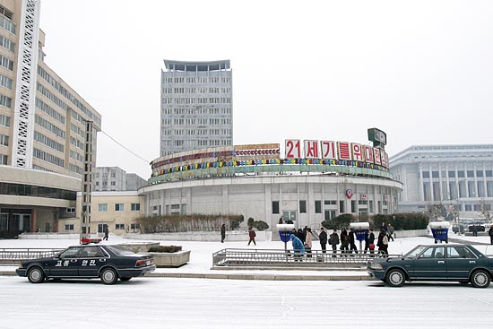 구호가 적힌 상점건물의 모습. 상점건물 앞에는 교통정리 차량과 공중전화도 보인다. [사진-통일뉴스 김주영 기자]
