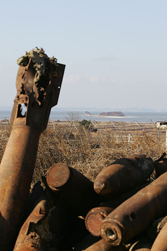 '매향리주민대책위' 사무실 앞에 쌓인 포탄들 너머로 농섬이 보인다. [사진-통일뉴스 김주영 기자]