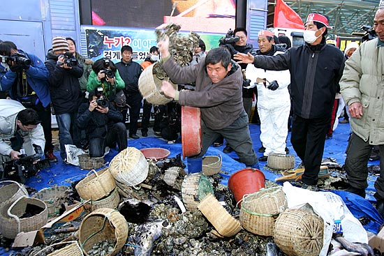집회 도중 분노한 어민이 가져온 굴과 조개 등 기름을 뒤집어 쓴 해산물을 집어 던지고 있다. [사진-통일뉴스 김주영 기자]