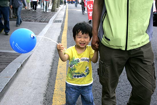 검게 그을린 아버지의 손을 잡고 거리행진에 참가한 어린이.[사진-통일뉴스 조성봉 기자]