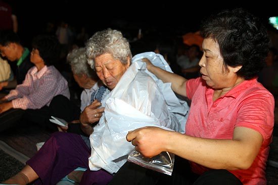 촛불문화제가 진행되는 가운데 비가 오자 할머니에게 우비를 입혀주고 있다.[사진-통일뉴스 조성봉 기자]