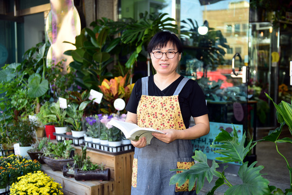 류이경 작가는 꽃집을 운영하고 있다. 작가가 꽃집 앞에서 단편소설 가 수록된 월간 한국소설(2021년 9월호)을 들고 활짝 웃고 있다. [사진-통일뉴스 임재근 객원기자]