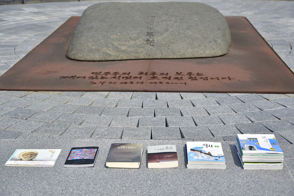 너럭바위 앞에 헌정된 4.3관련 책과 보고서들. 왼쪽부터 「무명천할머니」, 「틀낭에 진실꽃 피엄수다」, 「제주4‧3사건 추가 진상 조사 보고서」, 「4‧3의 진실을 찾아서」, 4.3사건이 담긴 중등 역사교과서 개정판이다.  [사진-통일뉴스 임재근 객원기자]