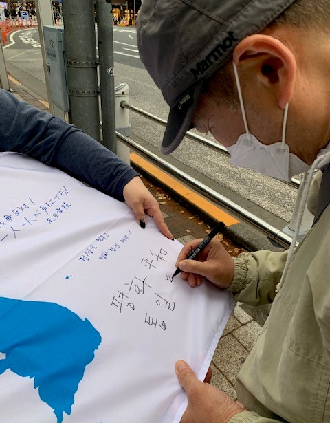 통일기 서명운동에서 한 일본인이 통일기에 '평화' '통일'이라고 쓰고 있다. [사진-통일뉴스 박명철 통신원]
