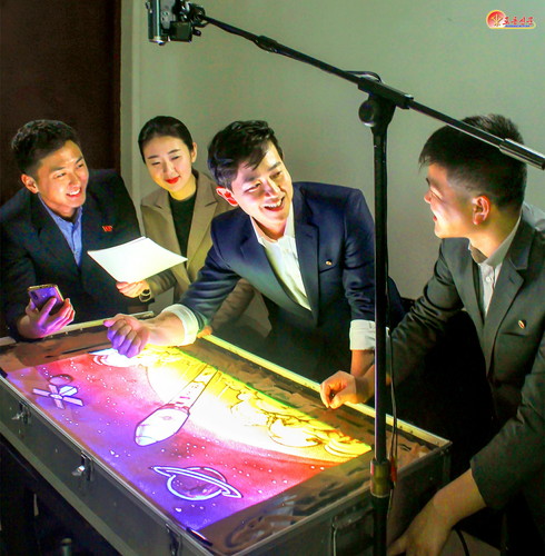 '만리경-1’호를 모래그림으로 그린 만수대창작사 출판화창작단 모래그림창작실의 창작가들.  [사진-노동신문 갈무리]