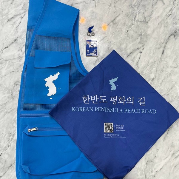 평화통일의 문이 열리길 소망하는 '2026년 통일걷기' 참가자들을 위한 조끼와 손수건, 뱃지. 뱃지 됫면에 새긴 '언약은 강물처럼 흐르고 만남은 꽃처럼 피어나리' 문구가 간절함을 더한다. [사진-이인영 의원 페이스북]
